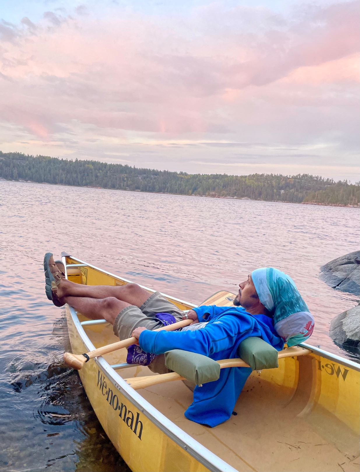 Derick Lugo rests in a canoe on a lake wearing Oboz Whakata trail sandals.