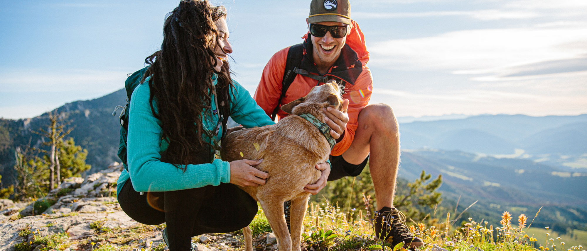 Two hikers petting a dog in the mountains on a hike.