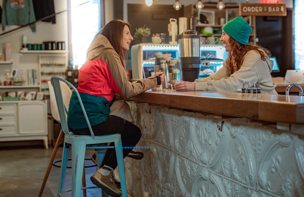 A woman sitting at a counter in a coffee shop wearing Oboz boots