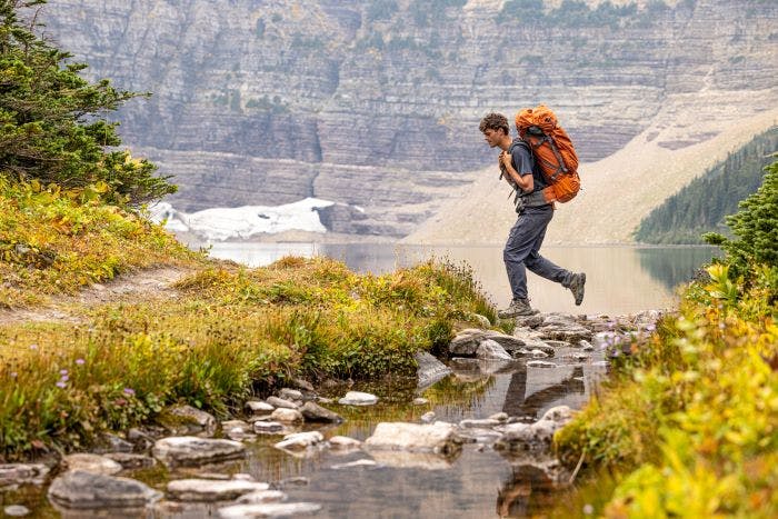 A hiker walks across a creek during a trek in the mountains in Oboz hiking shoes