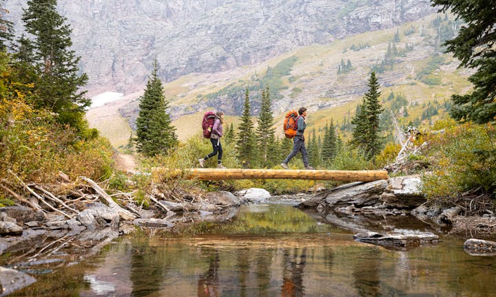 Two hikers cross over a mountain creek in Oboz hiking boots while backpacking in Montana.