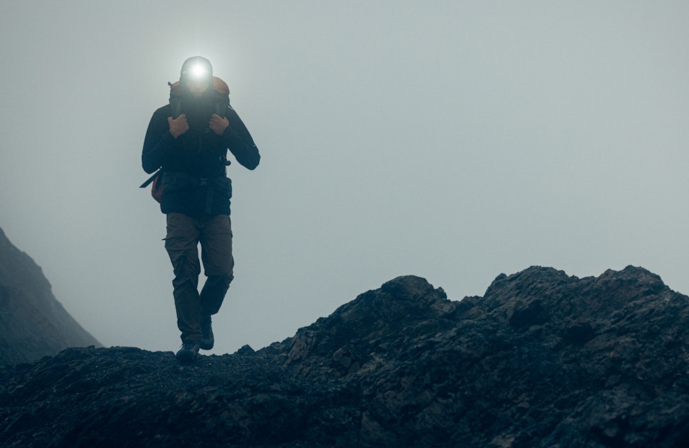 Backpacker with a headlamp in foggy conditions on rocky terrain.
