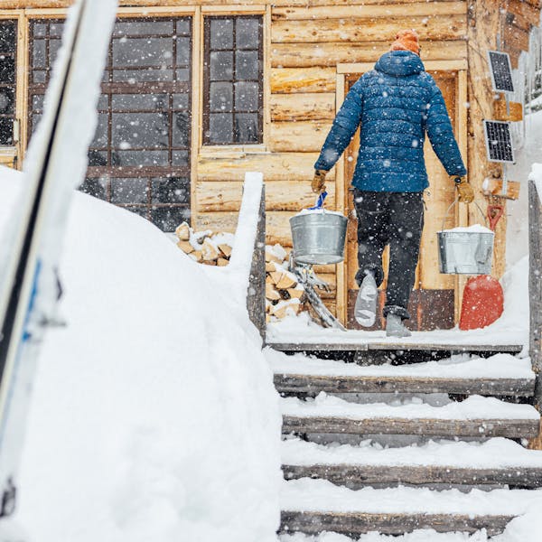 Man carrying buckets of snow wearing Oboz Whakatā Puffy Mid slipper shoes.