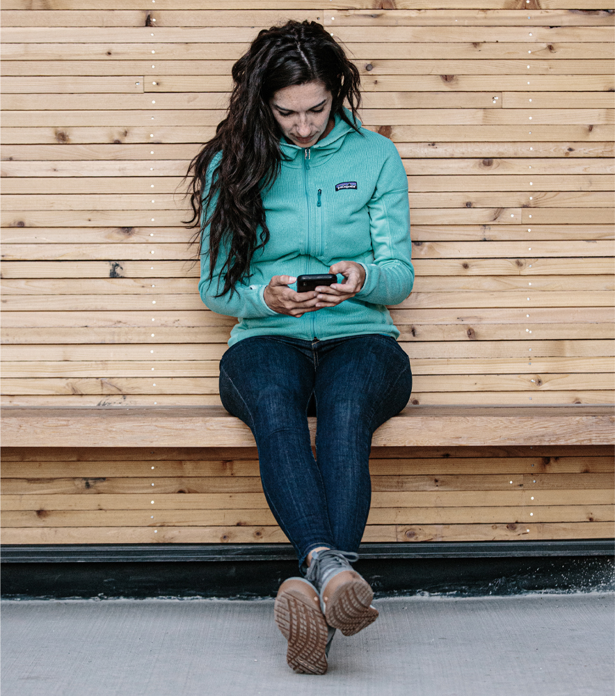 Jackie Nourse sitting on a bench on her phone wearing her Oboz shoes