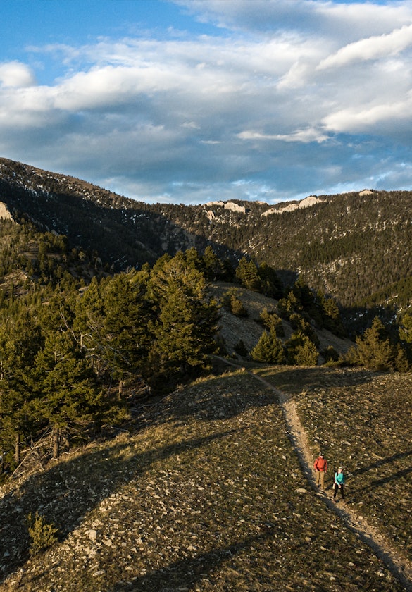 Two hikers in Montana mountains walking up a dirt trail in Oboz hiking boots.