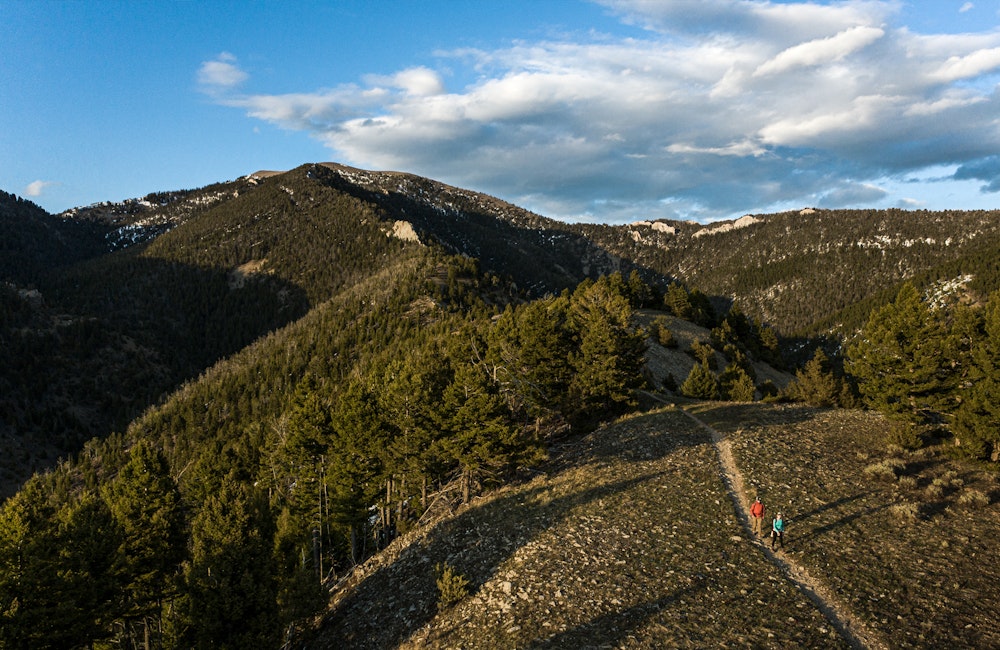 Two people hiking on trail under blue skies wearing Oboz hiking shoes