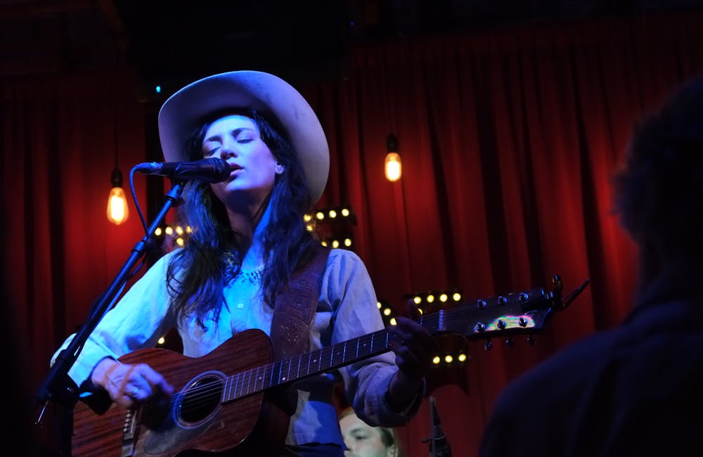 Musician wearing a cowboy hat while performing a song with a wooden guitar.
