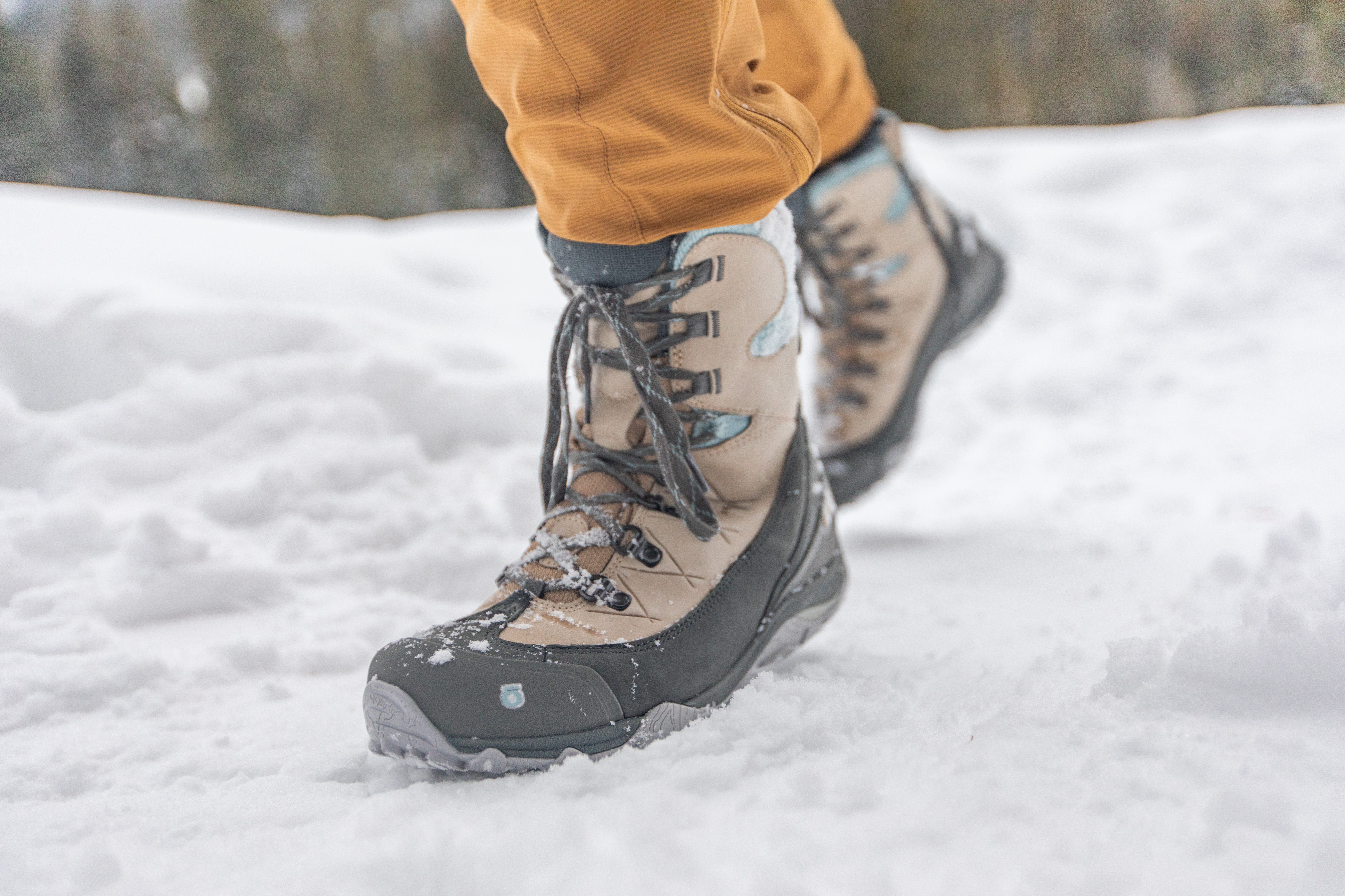 Oboz Ousel insulated winter boots walking over a hard packed snowy trail.