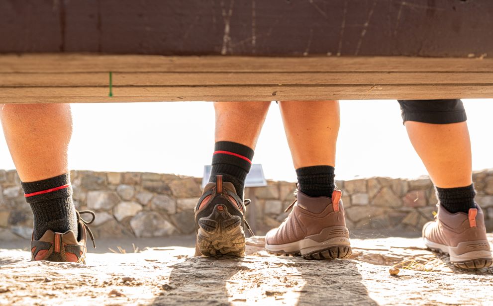 Two pairs of feet sitting on a bench in Oboz hiking boots.