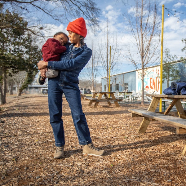 Woman stands holding a child at a picnic table wearing Oboz Hazel casual shoes.