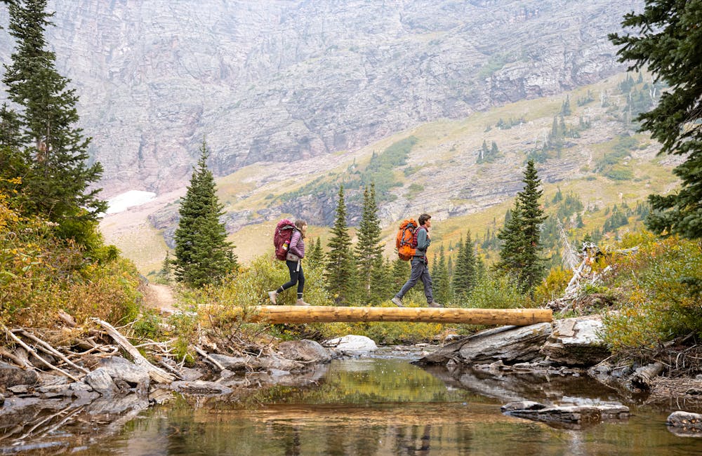Two backpackers walking across a log bridge in Oboz Sawtooth X hiking boots.