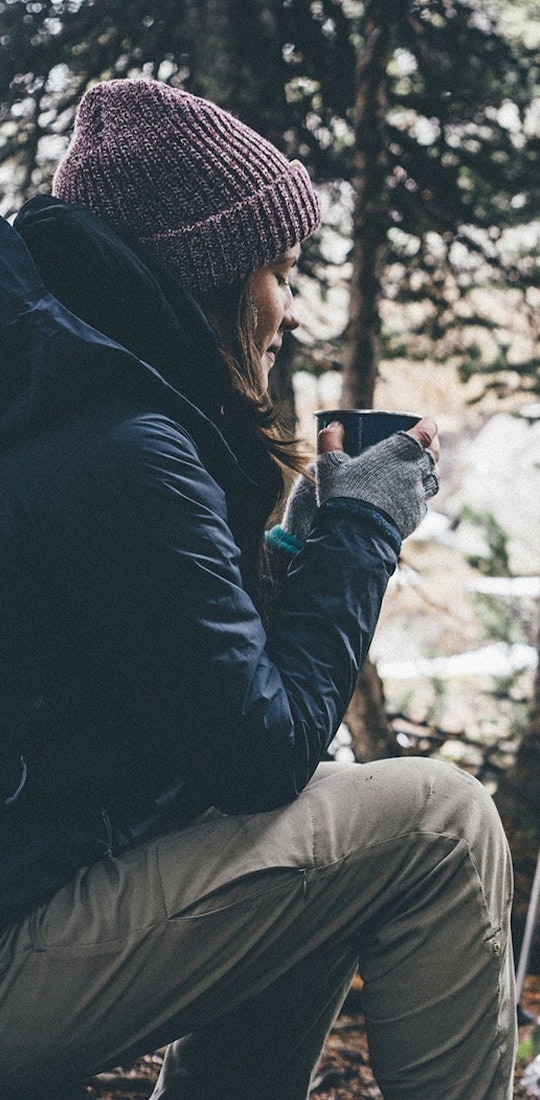 Woman camping in the woods and drinking coffee in the morning by her tent.