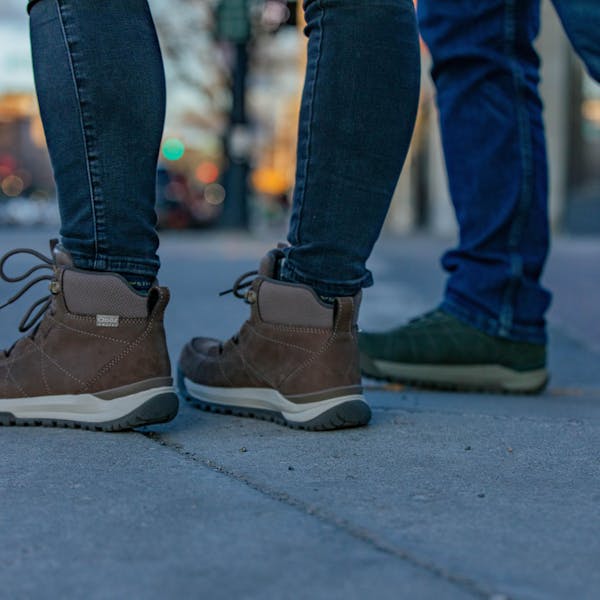 Two people in Oboz winter boots wait at a crosswalk cross the street.