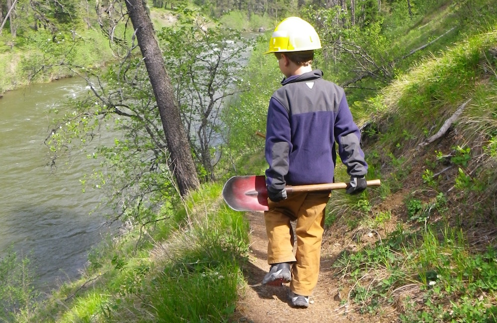 A young volunteer with a shovel working on a hiking trail in the Montana wilderness.