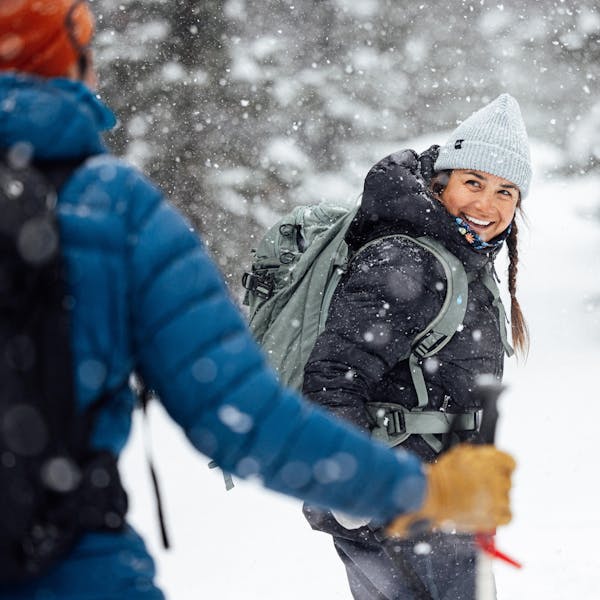 Two hikers in Oboz winter boots out snowshoeing on a snowy forest trail.
