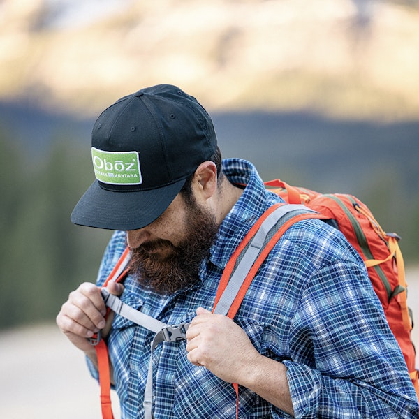 Man adjusting his backpack chest strap while hiking in an Oboz Footwear hat.