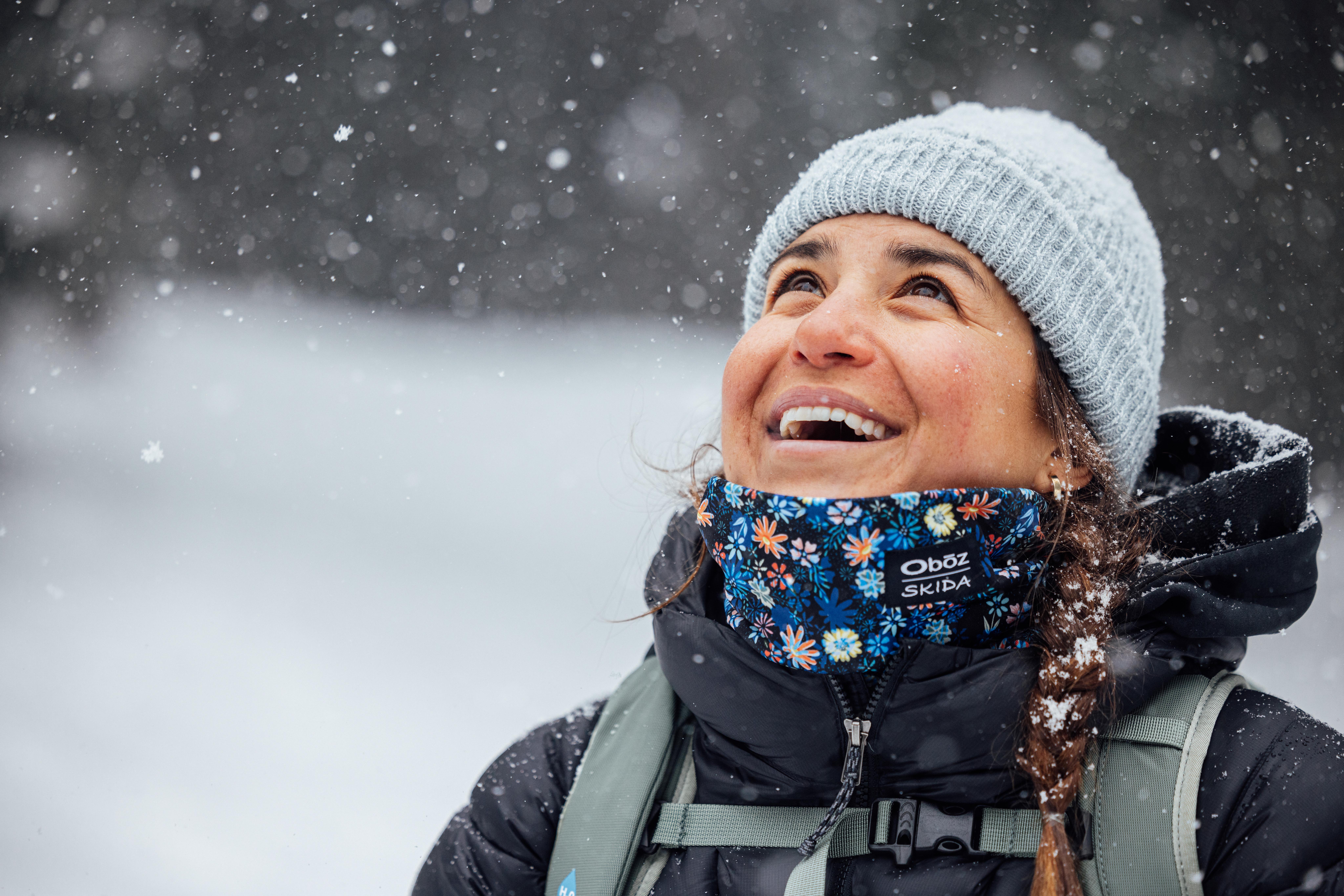Woman laughs in the snowy winter weather while hiking in an Oboz X Skida neck warmer.