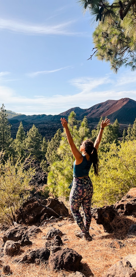 Woman on a trail soaking up the sun with her arms up in the air.