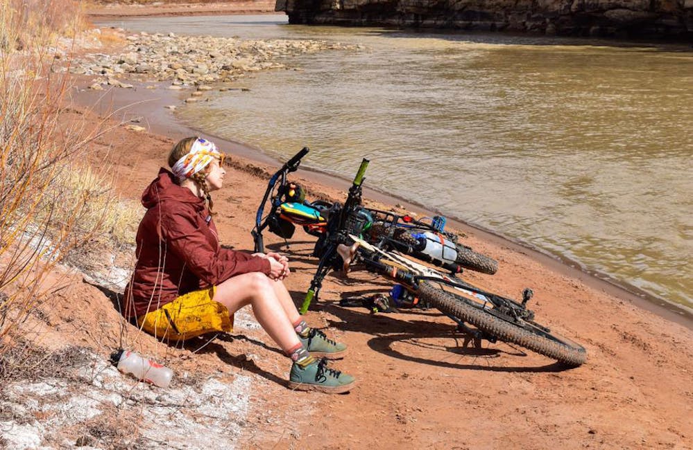 Oboz Trailblazer Ayla Mae Wild taking a break on a riverbank while biking.