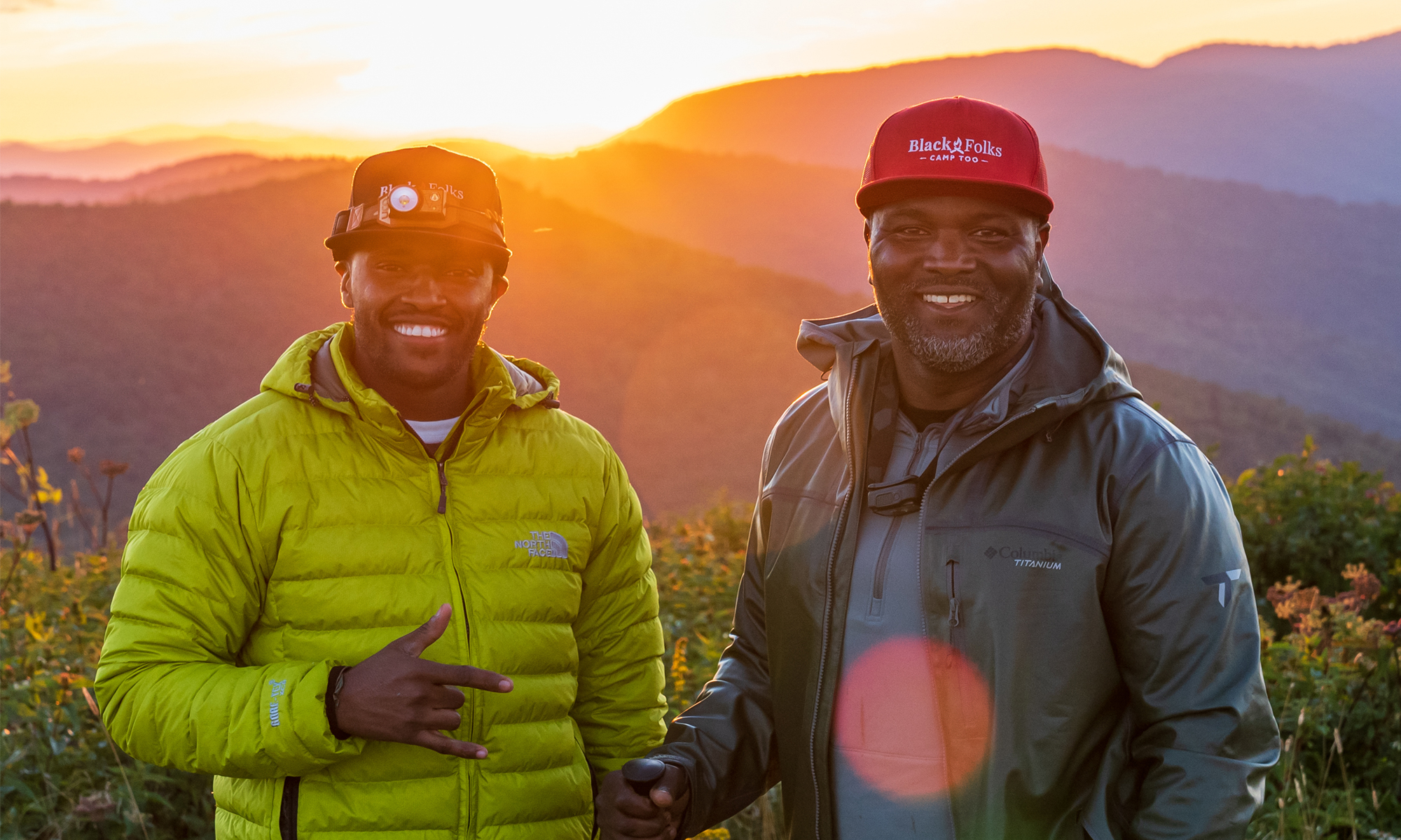 Two hikers with Black Folks Camp Too hats enjoying a beautiful Sunrise in the mountains.