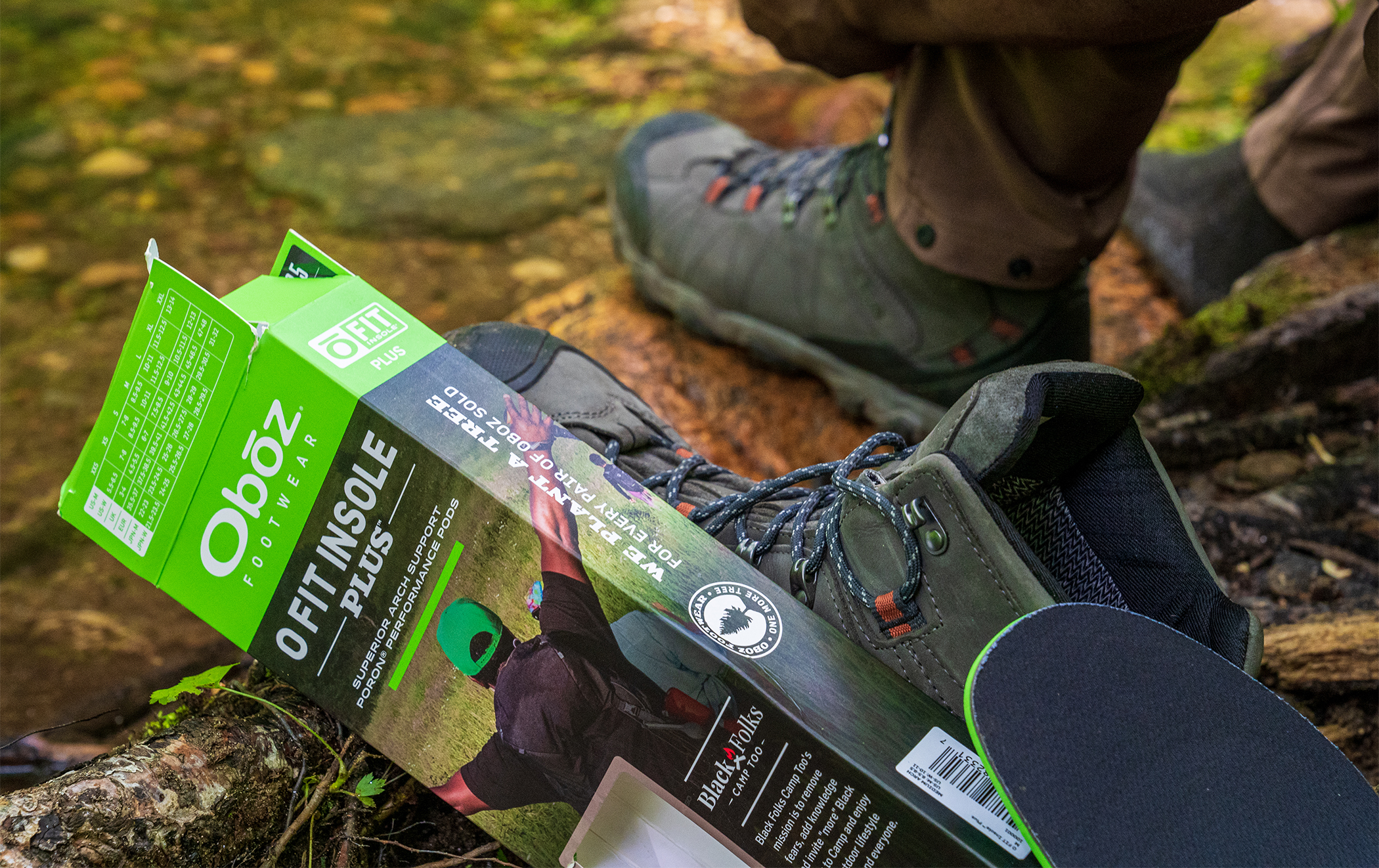 Oboz Black Folks Camp Too insole box near a creek bed.