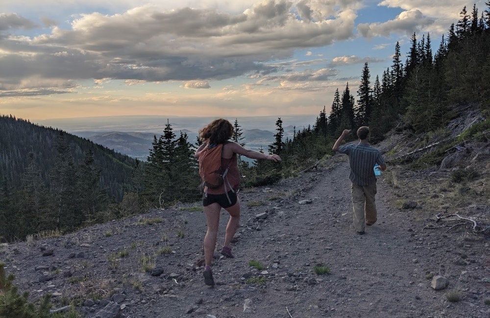Two hikers skipping on trail as the sun sets 