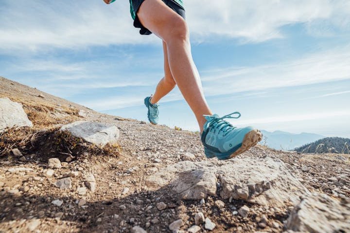 Person running in Oboz Katabatic trail shoes in blue on rocky terrain.