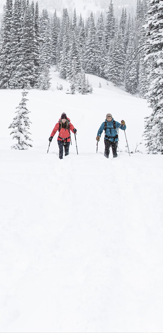 Two people snowshoe in in deep snow wearing Oboz Bridger Insulated hiking boots.