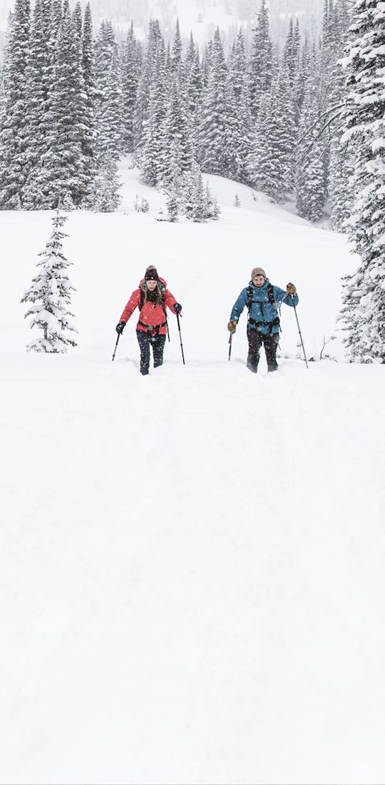 Two people snowshoe in in deep snow wearing Oboz Bridger Insulated hiking boots.