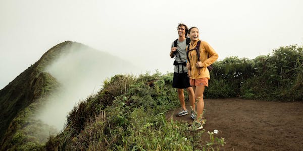 Two hikers at the top of a mountain top in the lush Hawaiian forest.