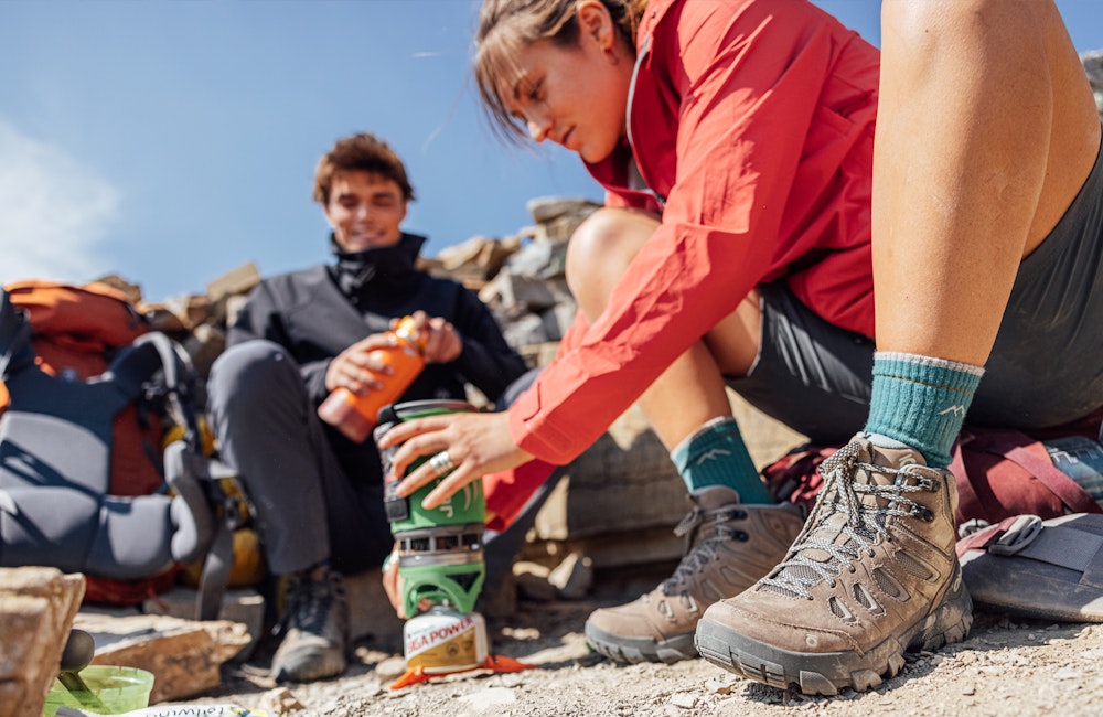 A woman cooks lunch on a backpacking trip in Oboz hiking boots