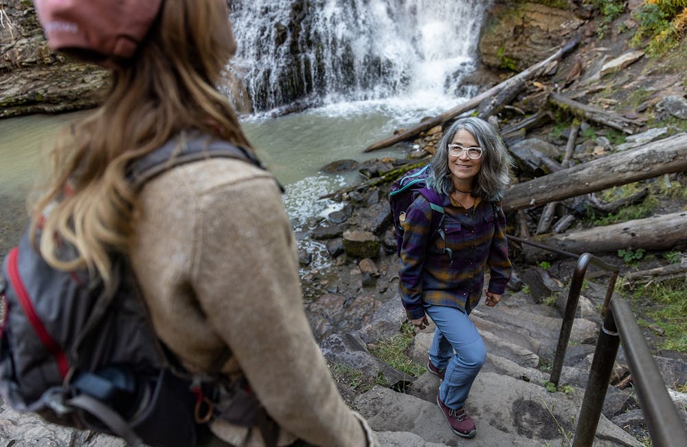 Two women wearing the Oboz Ousel hiking boots hiking at a waterfall near Big Sky, MT.