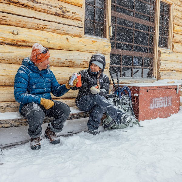 Two winter hikers smile and cheers beers while snowshoeing with Oboz boots on a snowy day.
