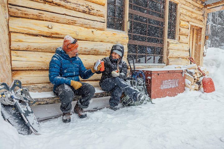 Two winter hikers smile and cheers beers while snowshoeing on a snowy day.