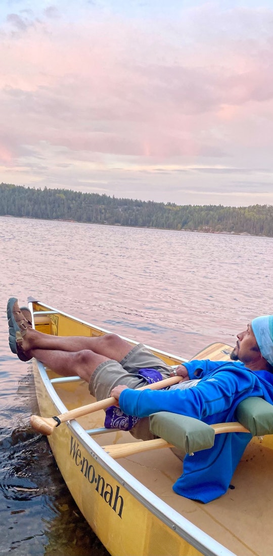 Derick Lugo rests in a canoe on a lake wearing Oboz Whakata trail sandals.
