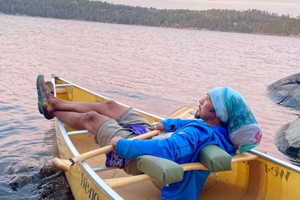 Derick Lugo rests in a canoe on a lake wearing Oboz Whakata trail sandals.