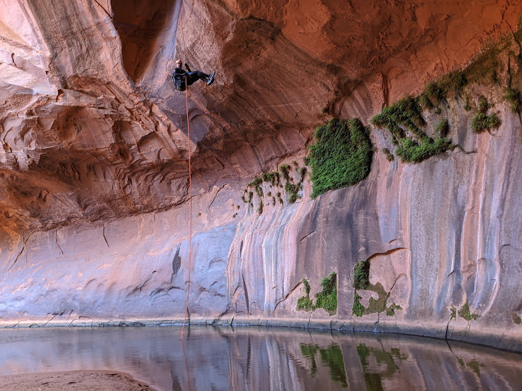 Human repelling down from a canyon wall toward a pool of water