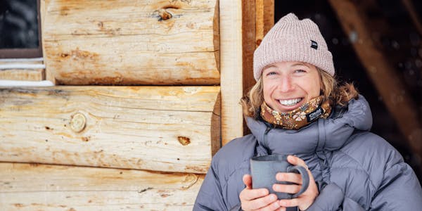 Corinne Prevot sipping coffee in a doorway wearing the Oboz and Skida Whakatā buff.