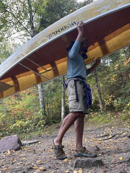 Person carrying a canoe over their head while on a backpacking trip. 