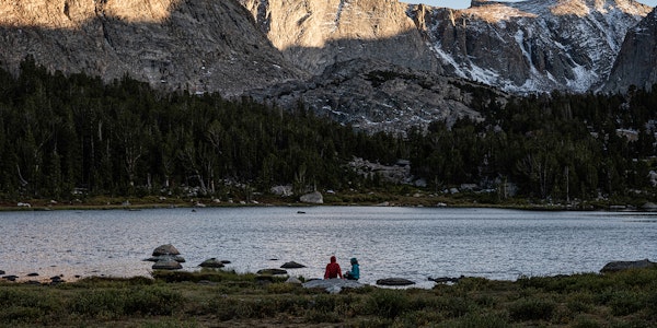 Two hikers having lunch at a mountain lake while wearing Oboz hiking footwear.