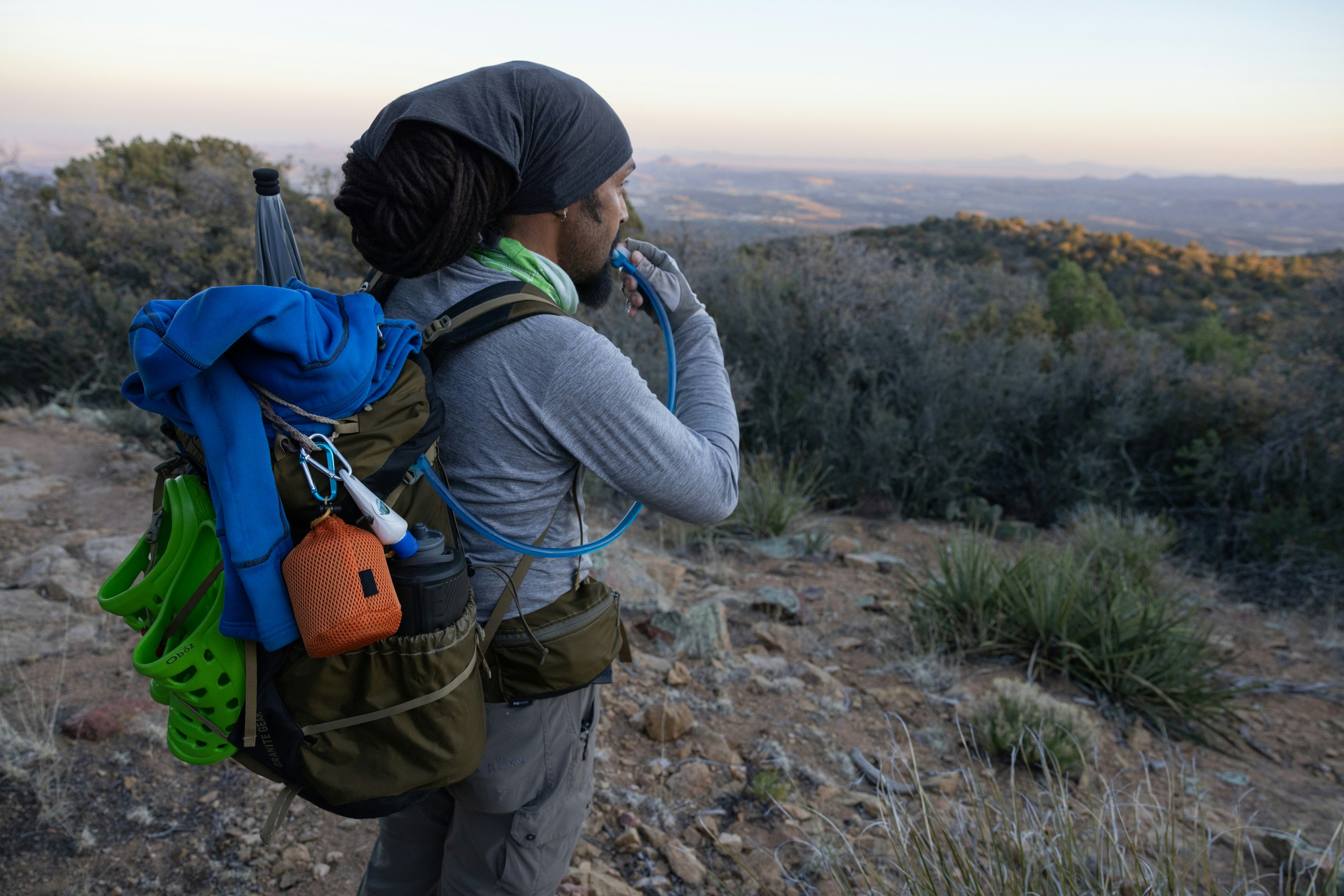 Derick Lugo drinking water out of his pack while thru hiking on a desert trail of the Continental Divide Trail