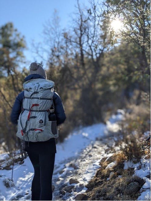 Hiker trekking through a snowy trail with a backpack during the winter time.