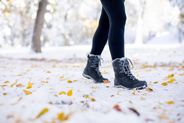 Woman wearing Oboz Ousel winter boots while walking on snow covered path in the fall.