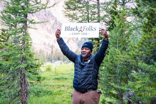 Earl Hunter Jr, founder of Black Folks Camp Too in the wilderness holding a BFCT sign.