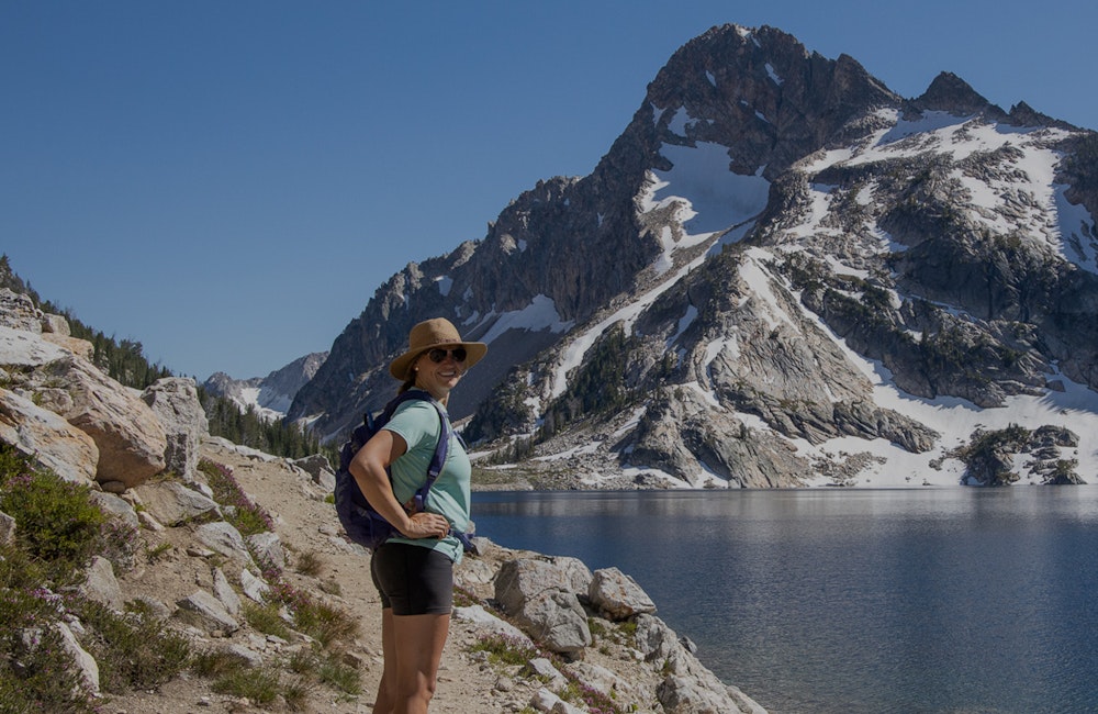 Hiker posed in front an alpine lake and snowy mountain wearing Oboz hiking shoes