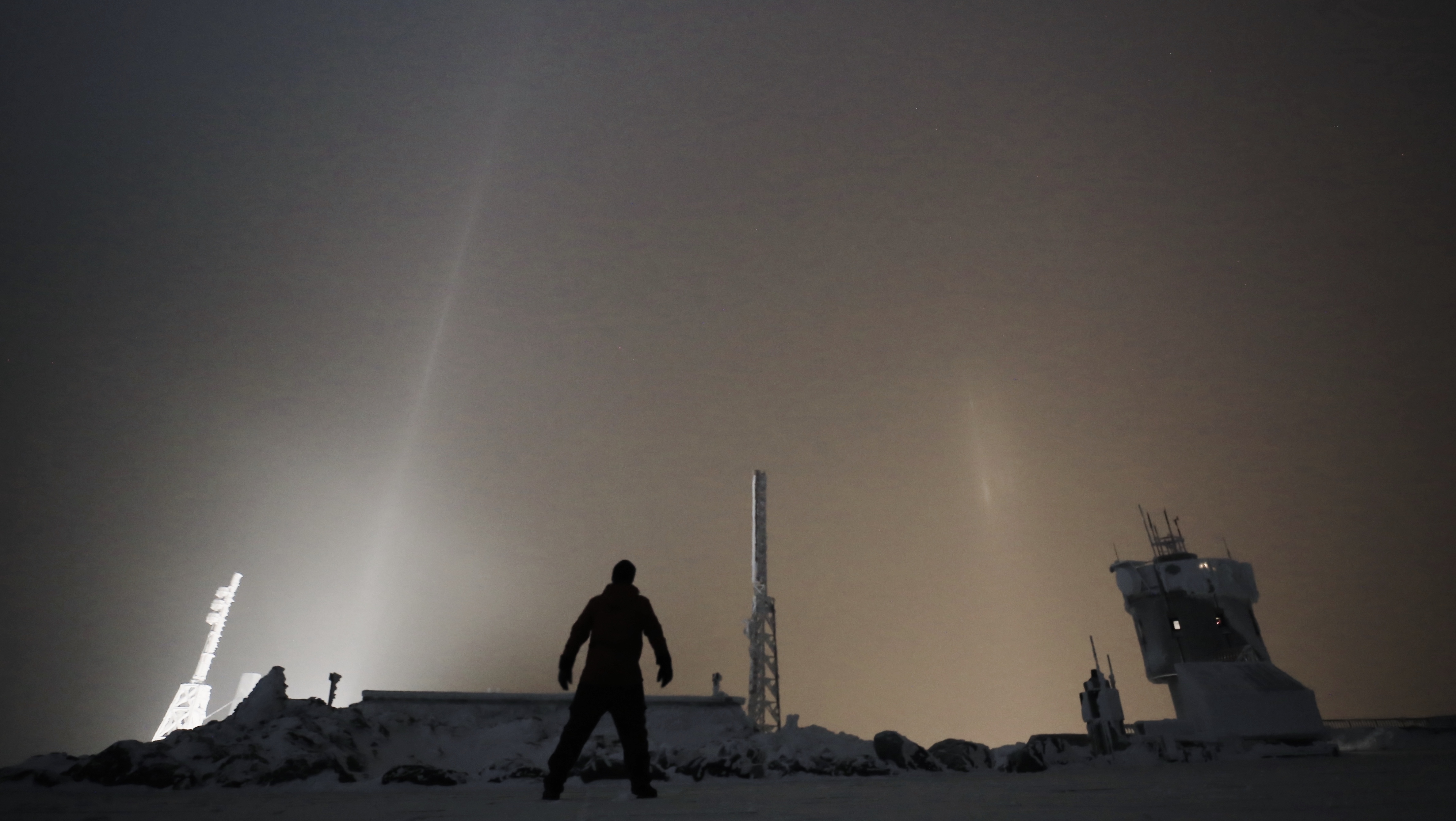 A person standing on the top of the Mt. Washington Observatory in winter at night.