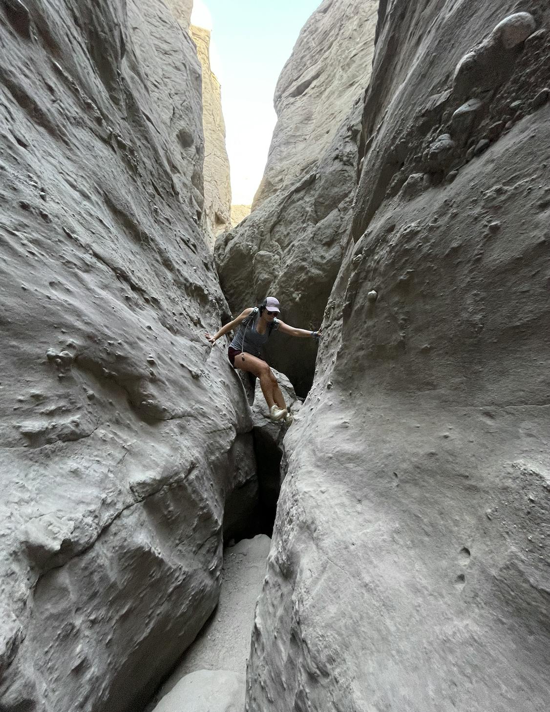 A hiker supports themselves in a slot canyon in the southwest