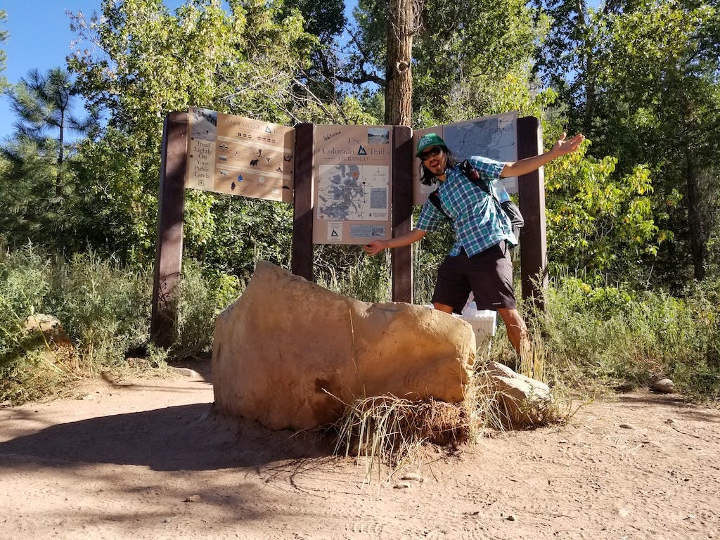 Tyler poses by a trail map on a hike through the forest