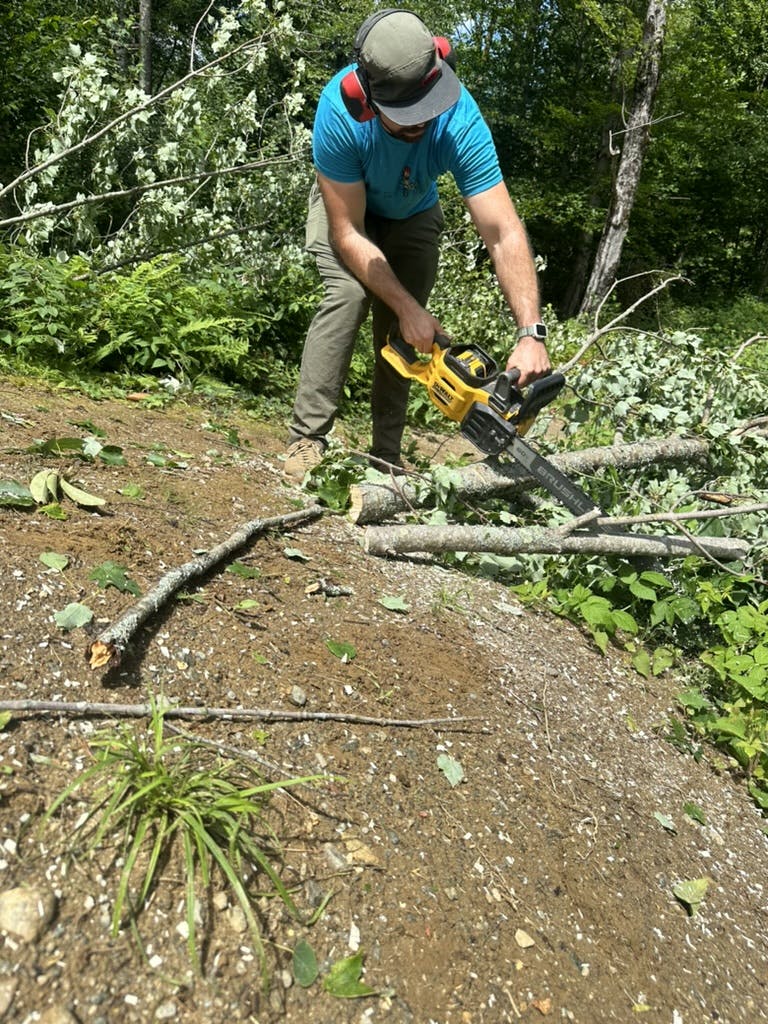 A trail builder uses a chainsaw to take downed trees off a trail.