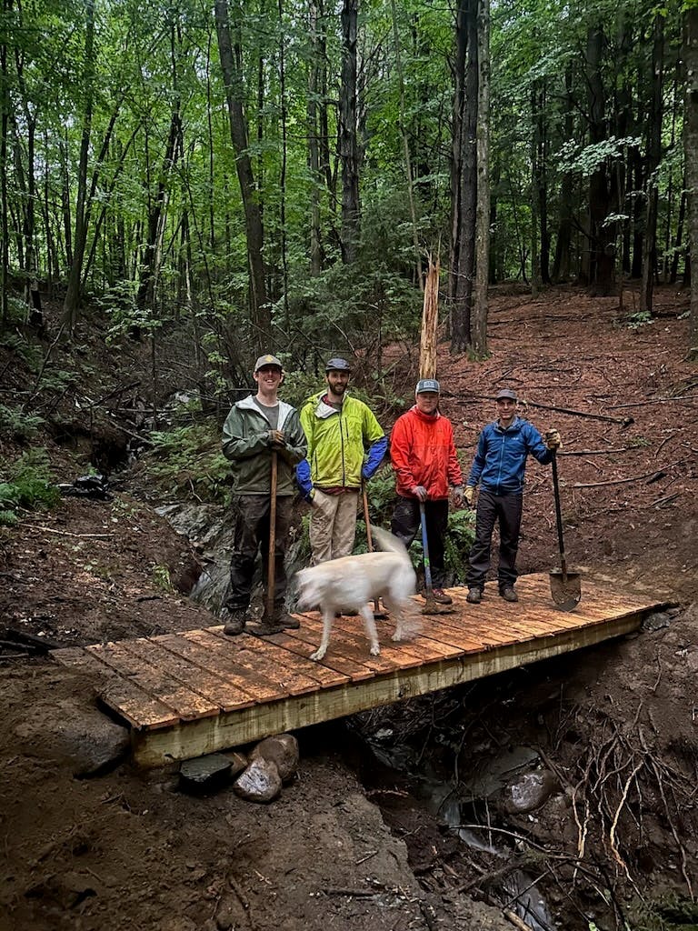 A group of trail builders stand on a bridge during a project in the North East.
